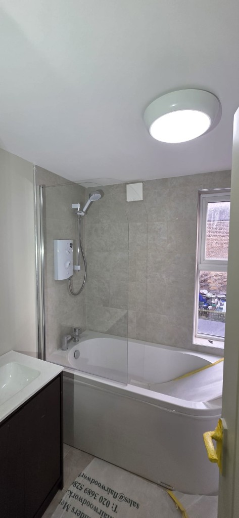 Bathroom refurbishment with white bath, glass shower screen and stone-effect tiling by Ikveles Construction