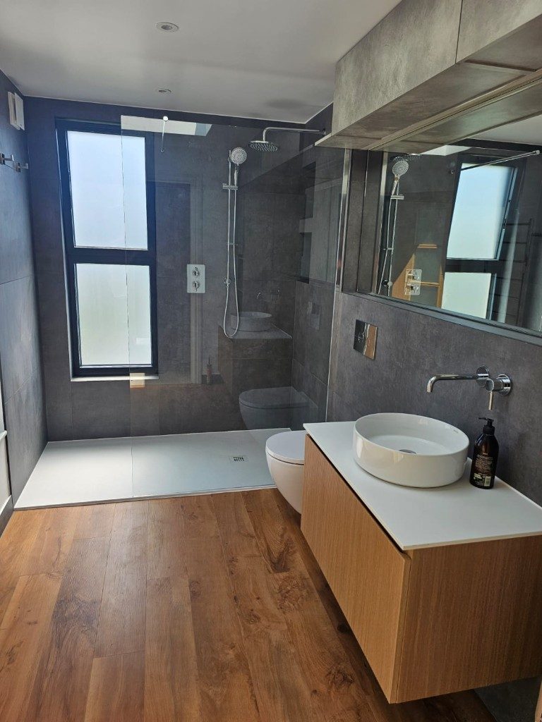 Modern bathroom refurbishment with charcoal tiles, wood vanity, vessel sink and glass walk-in shower by Ikveles Construction