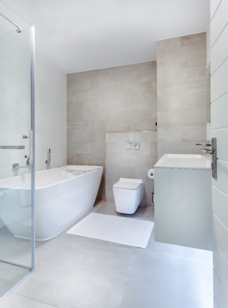 Modern bathroom refurbishment with freestanding bath, wall-hung toilet and grey tiling by Ikveles Construction