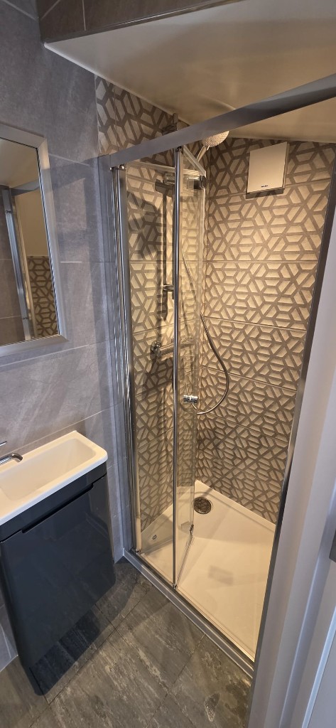 Modern bathroom refurbishment with geometric feature tiles, glass shower and charcoal vanity by Ikveles Construction