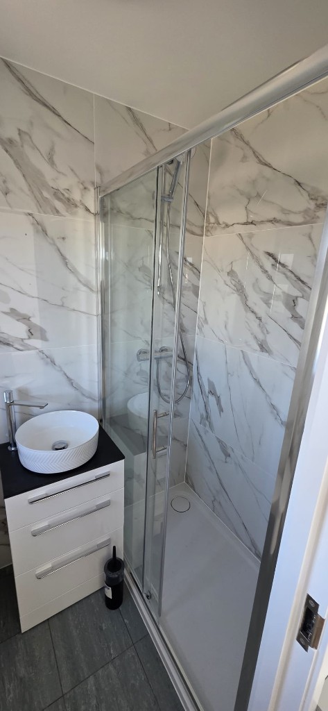 Bathroom renovation with marble-effect wall tiles, walk-in shower and vessel sink by Ikveles Construction