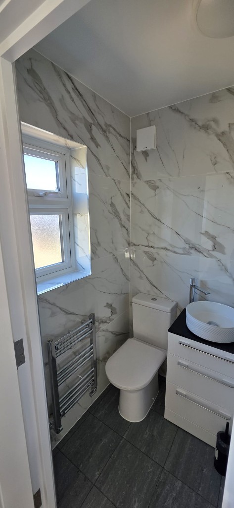 Small bathroom refurbishment with marble-effect tiles, white vanity and dark floor tiles by Ikveles Construction