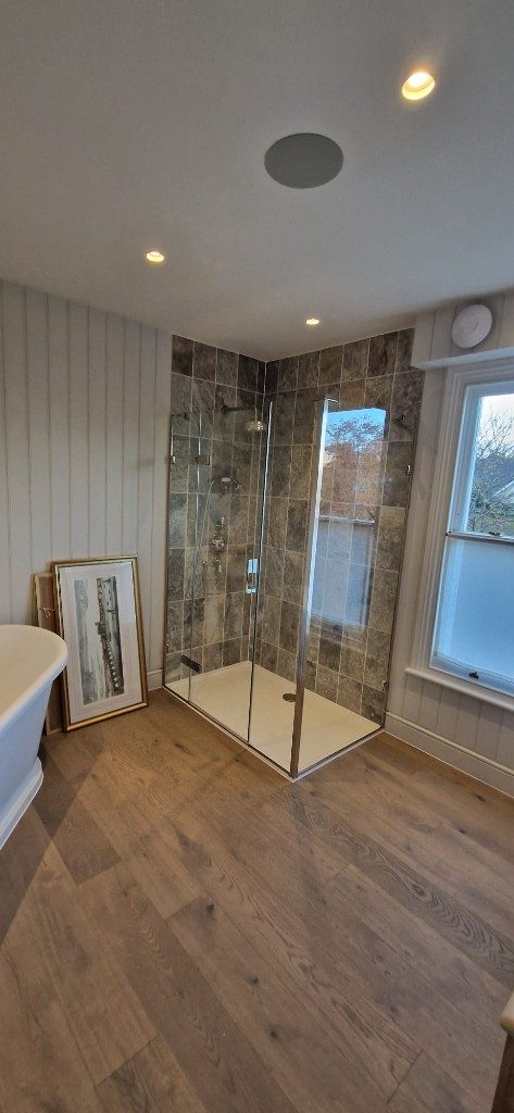 Bathroom renovation with stone-tiled glass walk-in shower, freestanding bath and wood flooring by Ikveles Construction