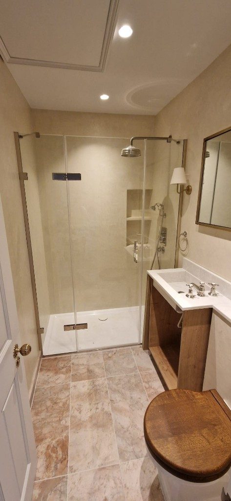 Bathroom refurbishment with frameless walk-in shower, marble floor tiles and wooden vanity by Ikveles Construction