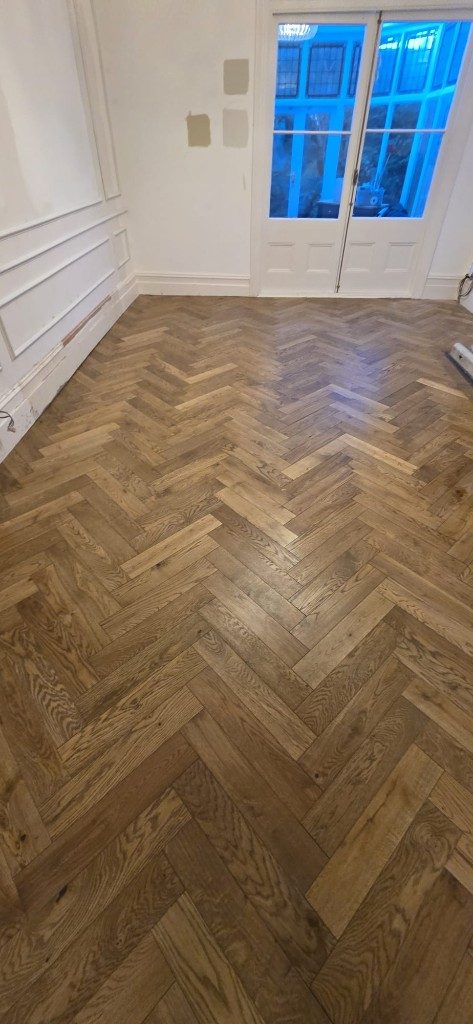 Completed herringbone wood flooring in a living room with paneled walls by Ikveles Construction