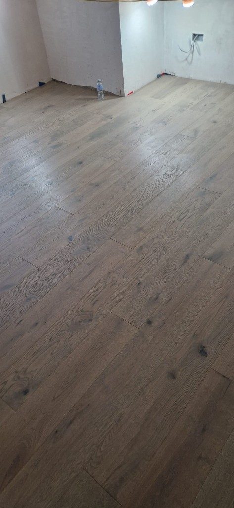 Wide-plank greige wood flooring freshly installed during renovation by Ikveles Construction