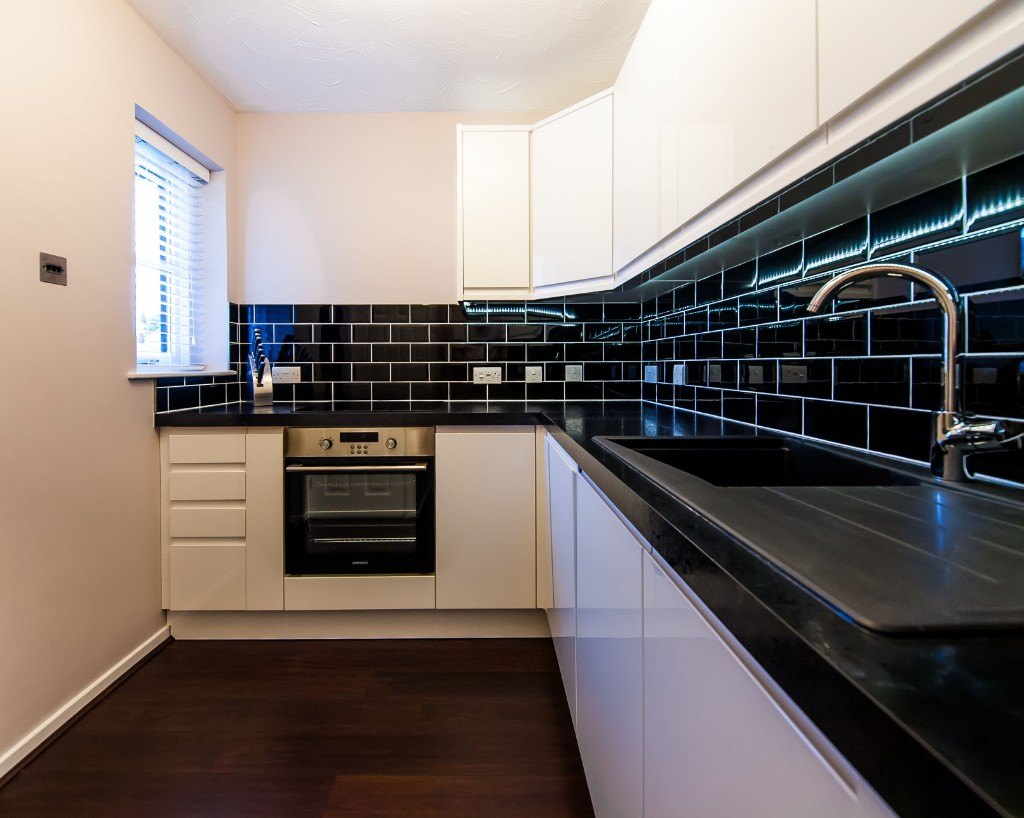 Kitchen after refurbishment with white cabinets, black worktop and tiled splashback by Ikveles Construction