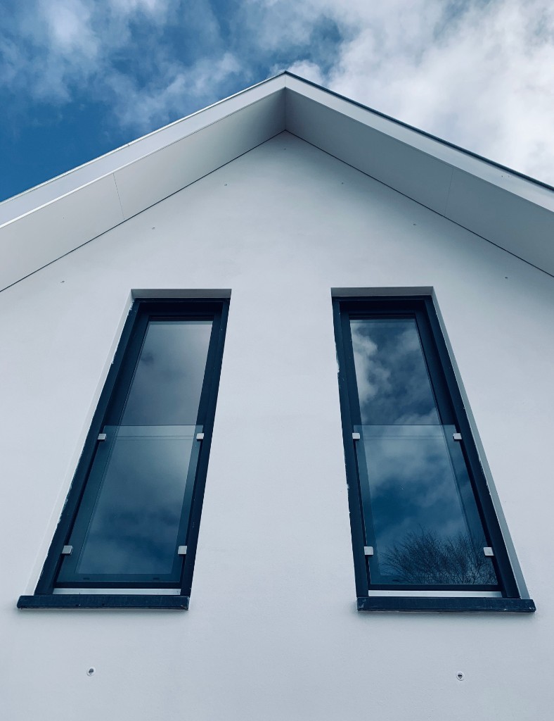 Modern white rendered house exterior with gable windows by Ikveles Construction