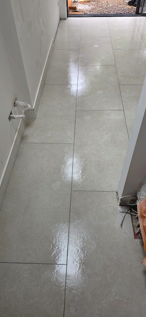 Large-format light stone-effect floor tile installation in a hallway by Ikveles Construction